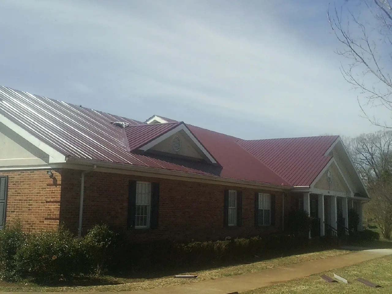 Red metal roof with gabled entries on a long brick building, from a Hail Damage Roof Repair job in Hector
