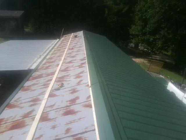 Old rusted panels beside newly installed green metal roofing — Wind Damage Roof Repair by Roofing Brothers in Hector