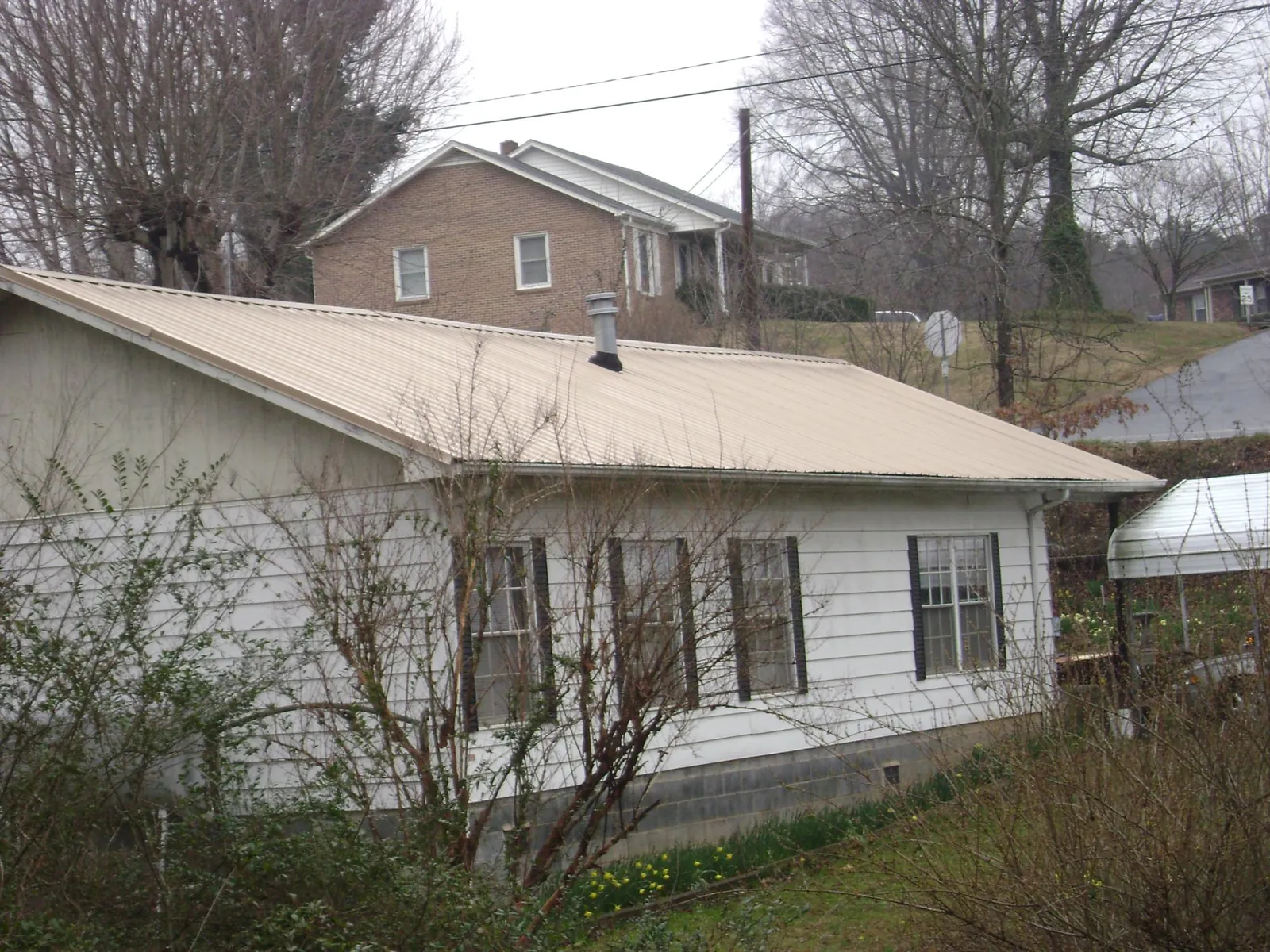 Tan metal roof on a white sided house set into a hillside — Commercial Roofing by Roofing Brothers in Hector